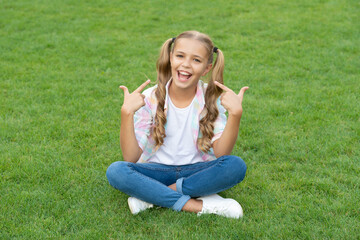 summer relax in park. teen girl sitting outdoor. childhood lifestyle of teen. relax on summer lawn. girl relax peacefully on the grass. happy childhood of teen girl. pointing finger on herself