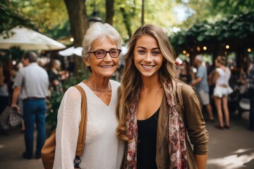 Portrait of loving adult daughter hugging middle aged mother from behind, looking at camera, happy mature grandmother and granddaughter posing together for family photo