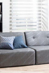 Luxurious Gray Modular Armless Sofa with Decorative Cushions in a Living Room, Illuminated by Natural Light from a Window with a Grey Cordless Blind, on Wooden Flooring - Vintage Light Filter
