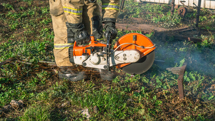 A lifeguard in protective clothing using a gasoline cutter with a cutting circle cuts a metal...