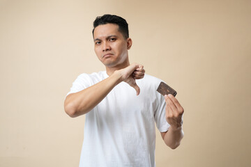 Photo of acne Problem Face man Eating Chocolate bar. Young man with acne problem eating chocolate bar. Isolated on beige background