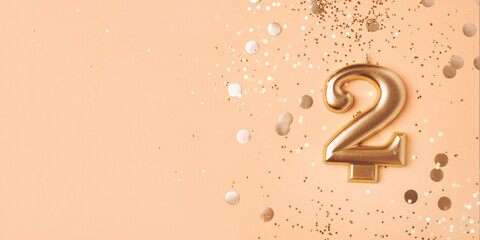 Gold candle in the form of number two peach background with confetti. - obrazy, fototapety, plakaty