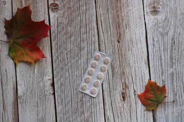a blister of tablets on a wooden background next to maple leaves