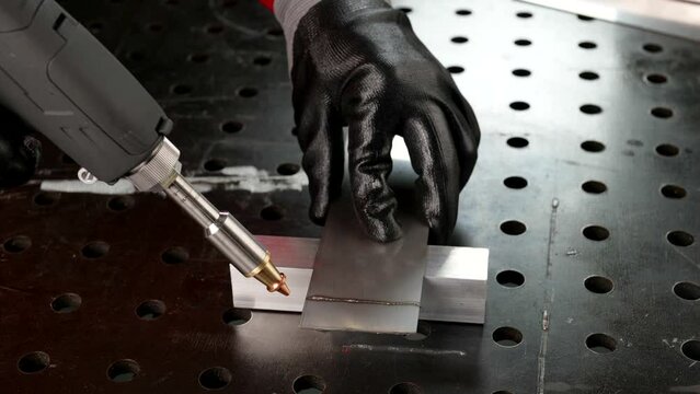 Laser welding machine with a hand gun. Laser cutting of aluminum metal is shown in close-up.