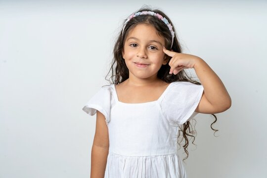 beautiful kid girl wearing dress tries to memorize something, keeps fore finger on temple, reminds information for exam,
