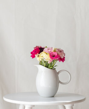 Vertical closeup of spring flowers in white jug on table against plain background with copy space