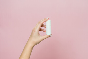 Hand holding white bottle. Drops for eye, nose or ear in hand on pink background. Pharmaceutical...