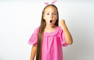 beautiful kid girl wearing pink dress angry and mad raising fist frustrated and furious while...