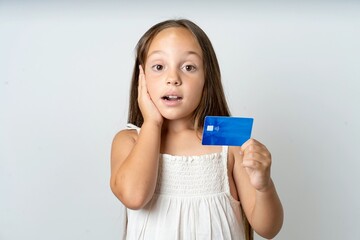 Astonished positive beautiful kid girl wearing white dress arm face hold bank plastic card...