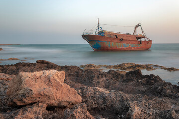 Fototapeta premium Rusty shipwreck on rocky beach with sky and ocean.