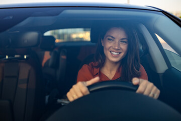Happy woman driving a car and smiling. Cute young success happy brunette woman is driving a car. Portrait of happy female driver steering car with safety belt - obrazy, fototapety, plakaty