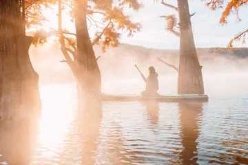 Foto op Canvas Woman relax on staand up paddle board at quiet lake with morning fog and fall Taxodium distichum trees © artifirsov