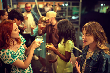Stylish young people, friends meeting in evening outdoors, on rooftop, drinking, talking, having fun together. Concept of party, leisure time, fun and joy, weekends, celebration, youth culture