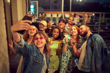 Group of young people, friends meeting on rooftop in evening, having good time together, taking selfie. Concept of party, leisure time, fun and joy, weekends, celebration, youth culture