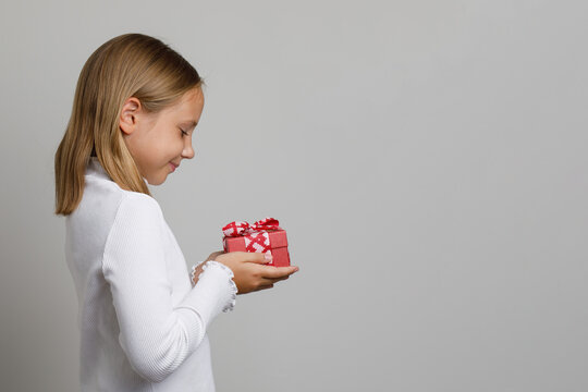 Adorable child girl holding red gift present box on white background, kid profile portrait