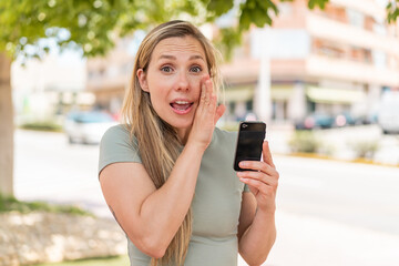 Young blonde woman using mobile phone at outdoors whispering something