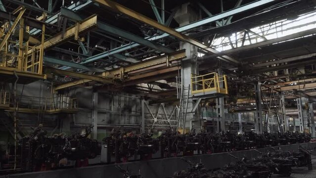 Dark assembly factory floor with automotive components and lifting mechanisms. Closed bankrupt factory without people. System of lifting mechanisms with powerful multi-ton hoists on beams.
