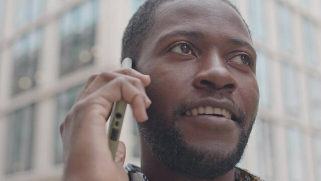 Medium closeup of smiling young African American man having phone conversation outdoors in urban environment at daytime