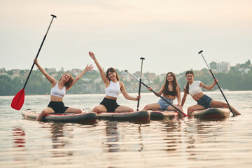 Friends are sitting and having fun. Young women are on sup boards in the lake