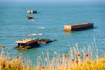 Remains of Phoenix caissons used to build the artificial Mulberry harbour on Gold Beach after the Normandy landings in World War II, seen from Cap Manvieux in Tracy-sur-Mer, France. - obrazy, fototapety, plakaty