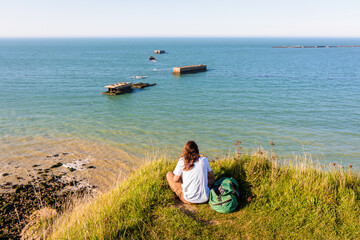 A young woman sitting at the Cap Manvieux in Tracy-sur-Mer, observes the remains of the Mulberry harbor, an artificial port built on Gold Beach after the Normandy landings in WWII.