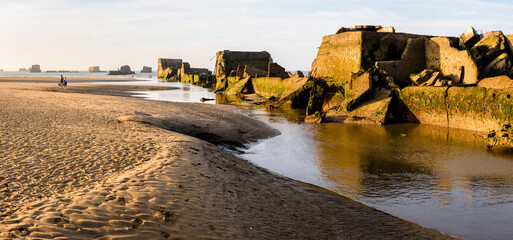 Remains of Phoenix caissons lying on the sand at low tide in Asnelles, France, used to build the artificial Mulberry harbour on Gold Beach after the Normandy landings in WWII. - obrazy, fototapety, plakaty