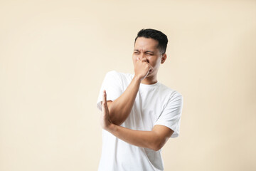 A photo of an Asian young man holding his nose against a bad smell, wearing a white t-shirt, and...