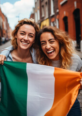 Obraz premium Two irish cheerful woman friends holding a Ireland flag on dublin city street