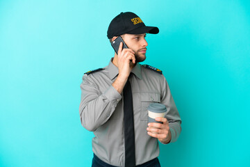 Young security man isolated on blue background holding coffee to take away and a mobile