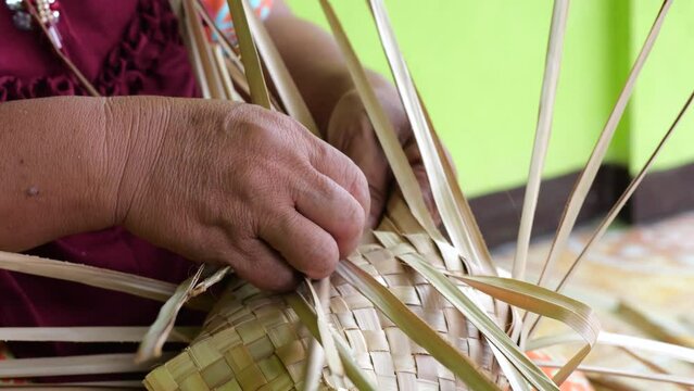 An Indonesian woman´s hand weaving an ancestral basket case from mangrove palm leaves . People is demonstrating weaving basket made from nipa palm. Weaving a traditional basket made from mangrove palm