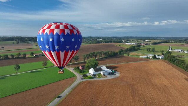 Aerial orbiting shot of american hot air balloon flying over golden wheat field at sunset time in american countryside