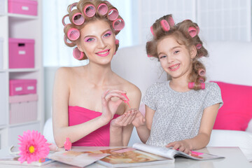 Obraz na płótnie Canvas Mom and daughter with hair curlers reading magazine