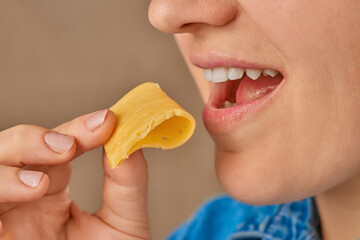 Close-up of a happy Caucasian woman holding a slice of cheese with her hand and bringing it to her...