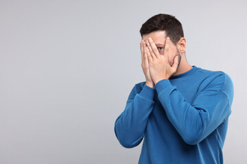Embarrassed man covering face on light grey background. Space for text