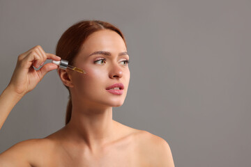 Obraz premium Beautiful young woman applying cosmetic serum onto her face on grey background, space for text