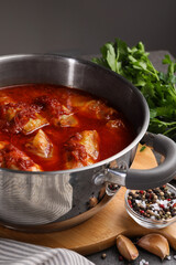 Delicious stuffed cabbage rolls cooked with homemade tomato sauce in pot and ingredients on table, closeup