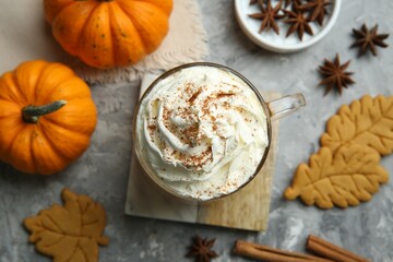 Fototapeta na wymiar Cup of pumpkin spice latte with whipped cream, cookies and ingredients on light grey table, flat lay