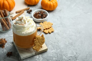 Cup of pumpkin spice latte with whipped cream, cookies and ingredients on light grey table. Space...