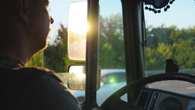Man driving truck and carefully watching the road. Caucasian guy is riding through countryside with beautiful landscape at background. Profile of lorry driver inside the cab. Slow motion Close up