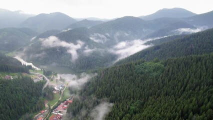 Sideway aerial pan of low hanging clouds above small village in the mountains. - Powered by Adobe