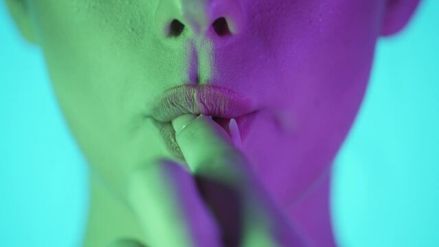 Static slow motion shot of beautiful young woman lips while she puts a sweet delicious gum in her mouth and starts chewing in front of turquoise background with green purple contrast on face