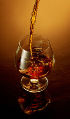 Close up top view image of pouring to glass whiskey, rum, brandy or gin over golden gradient background.