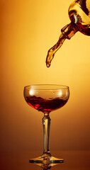 Photo of pouring whiskey, rum, brandy or gin from bottle to high glass over golden gradient...