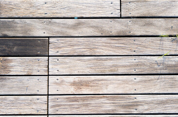 Exterior wooden deck planks aged by the passage of time with a very marked texture and a gray and light marks of screws and nails between the slats