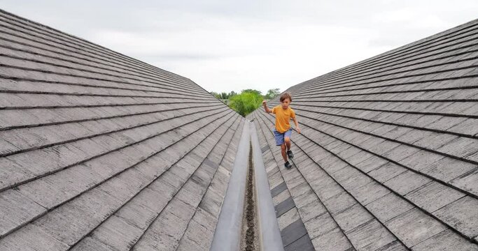 Little boy fearlessly runs and jumps between roof slopes towards us, demonstrating his agility and adventurous spirit. Slow-motion footage captures moments when he runs across sloping roof surfaces