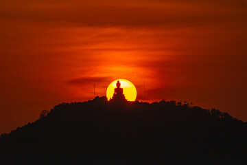 Fototapeta na wymiar The sun circles in the red sky behind the Big Buddha..Amazing Phuket big Buddha in circle of the sun in red sky..The beauty of the statue fits perfectly with the charming nature. .red sky background