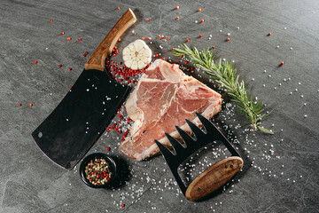Uncooked ribeye steak on the bone, sprinkled with salt and red pepper peas, lying on a stone table,...
