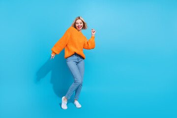 Full size photo of lovely gorgeous girl with blond hairdo wear knit orange jumper dancing enjoy party isolated on blue color background