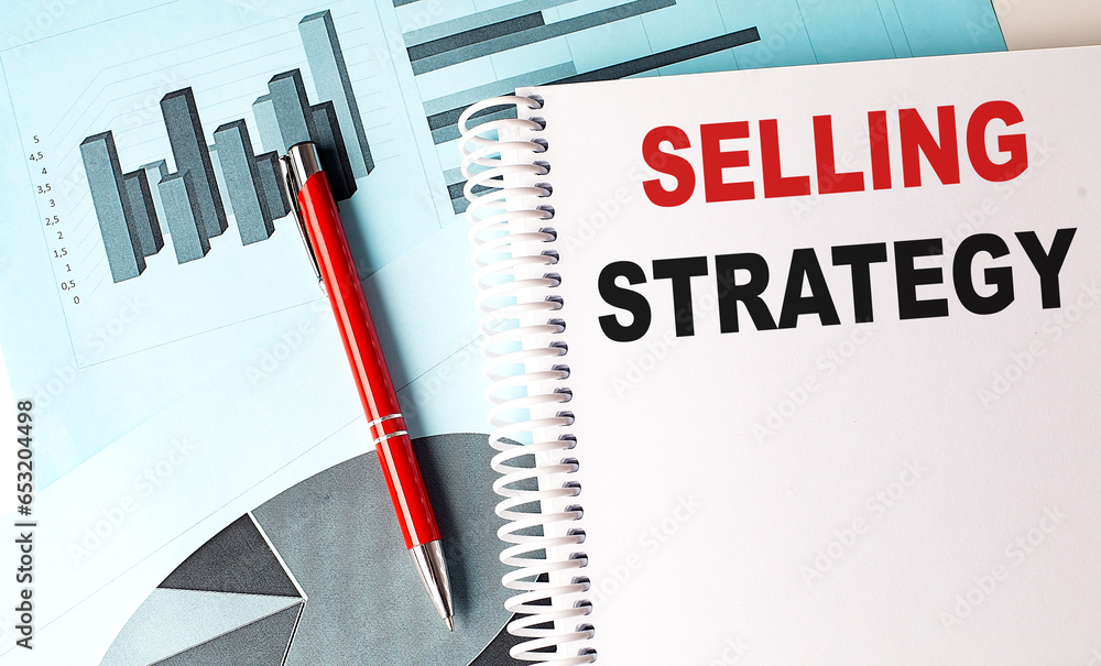 Aufkleber selling strategy text on a notebook with pen on a chart background