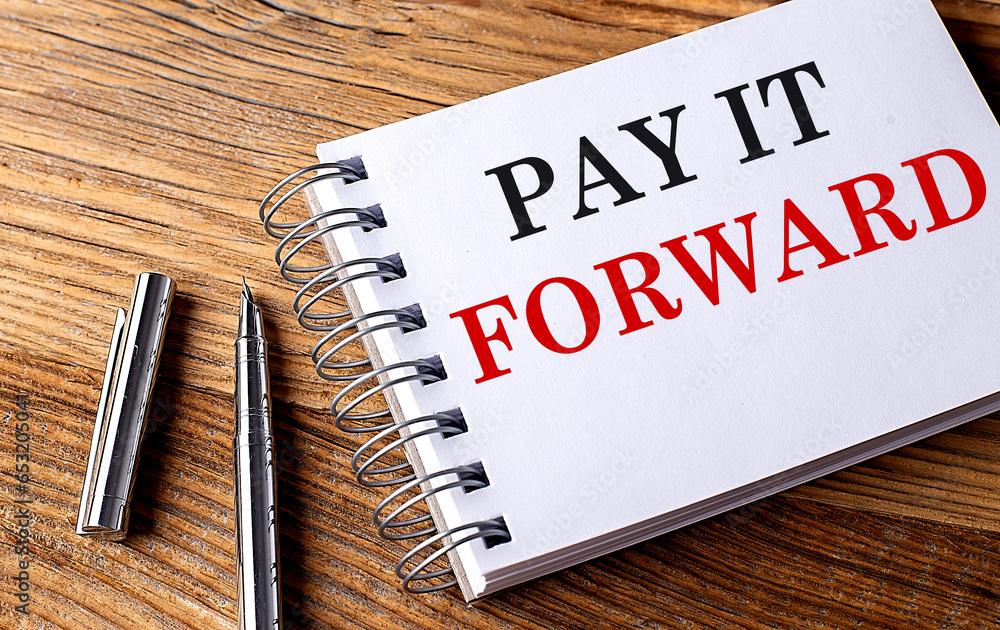 Poster pay it forward text on notebook with pen on wooden background